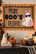A Halloween-themed wall sign with the text 'MORE BOO'S PLEASE' in black lettering on a tan background, bordered by orange and black stripes. The sign features a cartoon ghost wearing a pink bow, heart-shaped sunglasses, and holding a pink polka-dot drink and bag.