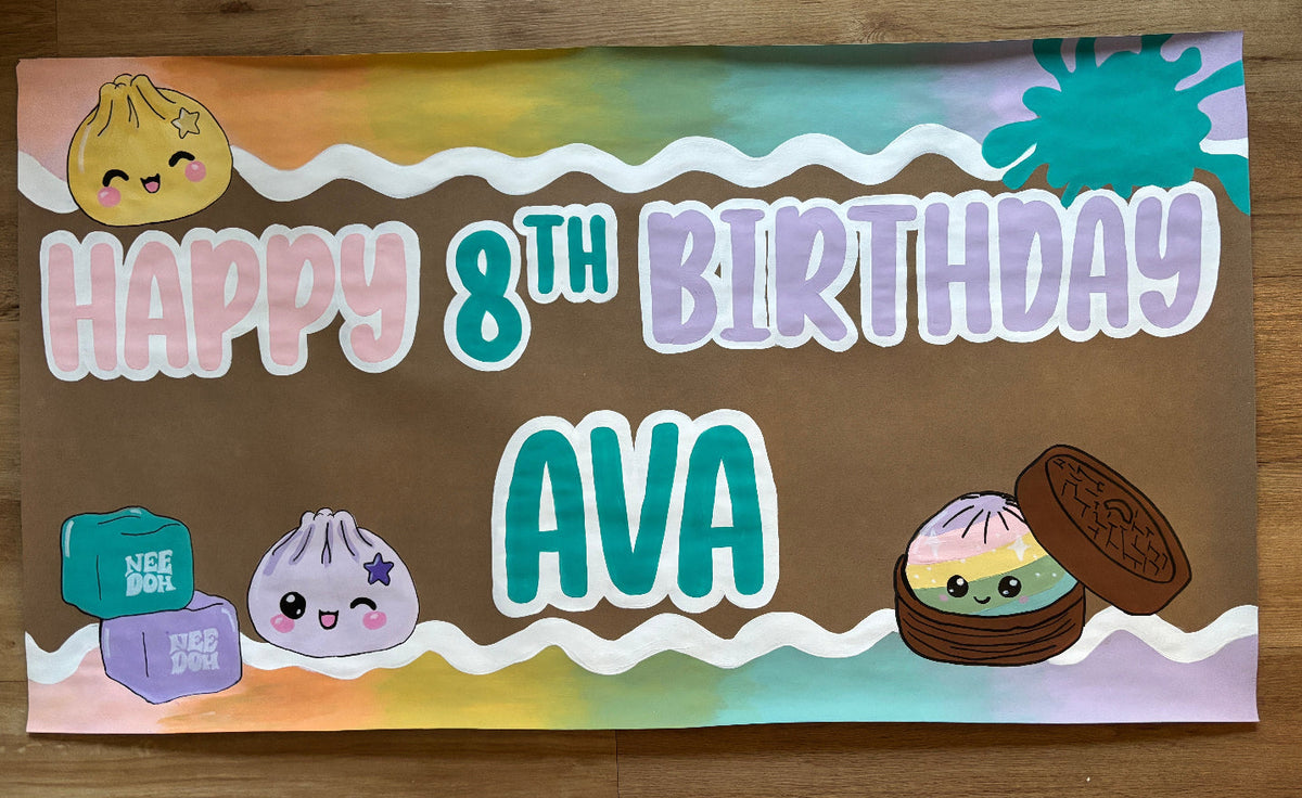 A rectangular custom birthday banner laid flat on a wooden floor. The banner features a brown center with wavy pastel stripes in orange, yellow, green, and purple, along with cute cartoon dumpling characters and the text 'HAPPY 8TH BIRTHDAY AVA'.
